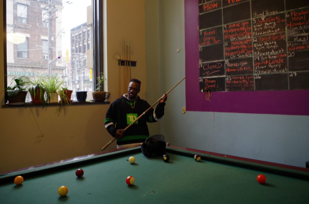 A participant plays pool at the Meeting Place in front of a schedule of activities